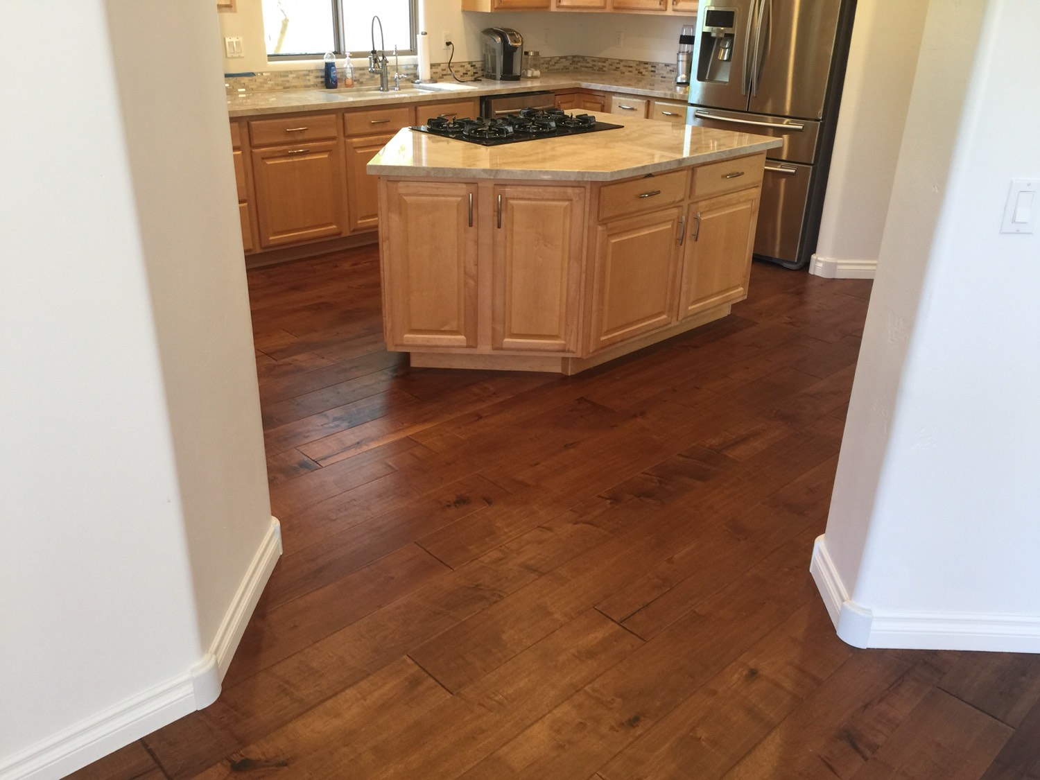 Hardwood floor running into a kitchen with an island and stone counters