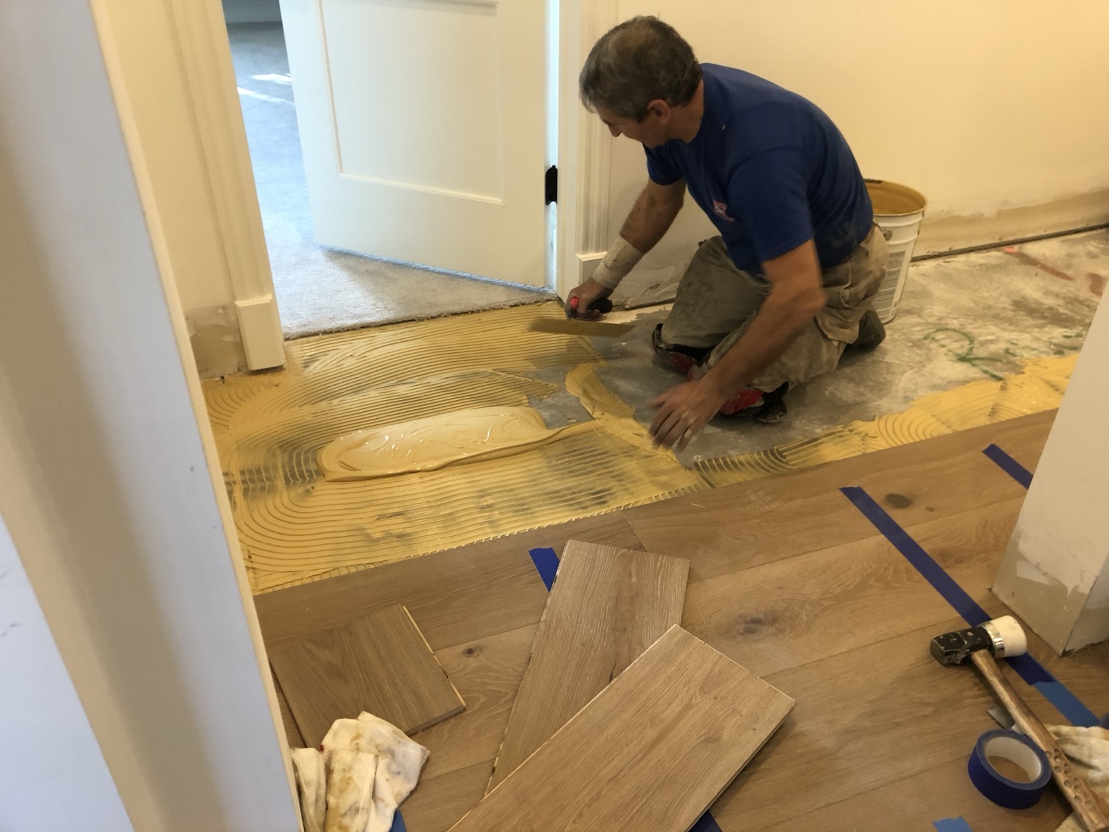 Olympic installer spreading adhesive and setting wide plank boards into a doorway